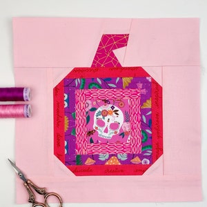 log cabin pumpkin quilt blocks in pink colors on pink background.log cabin pumpkin quilt block pattern in 5 different sizes, from 4x4 inch for ornaments to 6x6, 8x8, 10x10 and 12x12 inches for all sorts of amazing Halloween sewing projects. Use your favorite fabrics to fussy cut the center and turn these amazing beauties into your own pumpkin patch.