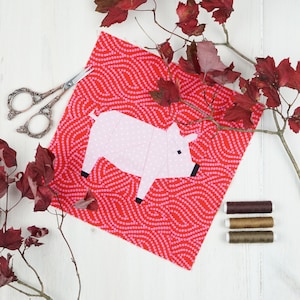 May include: A pink paper pig applique on a red fabric background with a white polka dot pattern. The fabric is surrounded by autumn leaves.