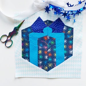 May include: A blue and white fabric hexagon with a blue and white patterned gift box design. The hexagon is surrounded by a white background with a light blue diamond pattern.