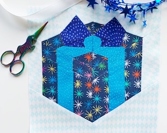 May include: A blue and white fabric hexagon with a blue and white patterned gift box design. The hexagon is surrounded by a white background with a light blue diamond pattern.