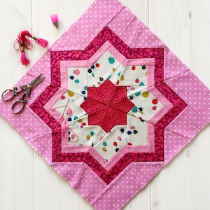 May include: A pink and white patchwork quilt block featuring a star design in the centre. The block is made up of various fabrics with different patterns, including polka dots, floral prints, and geometric designs.