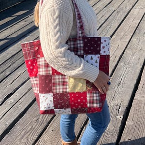 May include: A patchwork tote bag featuring a variety of red, white, and gold fabric squares with holiday-themed patterns including plaid, snowflakes, candy canes, and small Christmas trees, complete with two matching fabric shoulder straps.