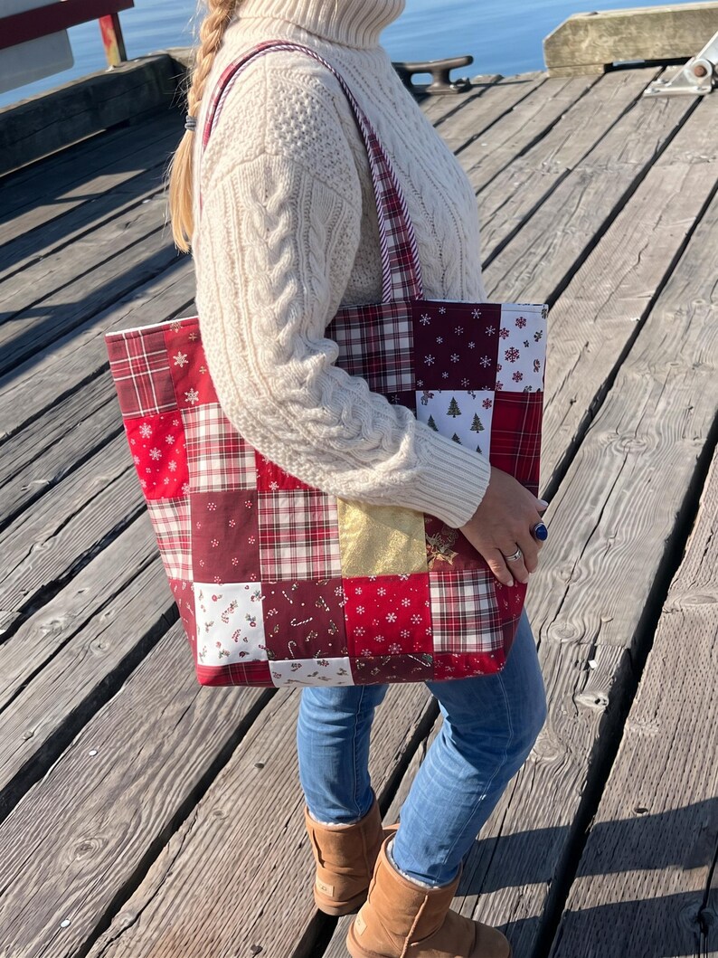 May include: A patchwork tote bag featuring a variety of red, white, and gold fabric squares with holiday-themed patterns including plaid, snowflakes, candy canes, and small Christmas trees, complete with two matching fabric shoulder straps.