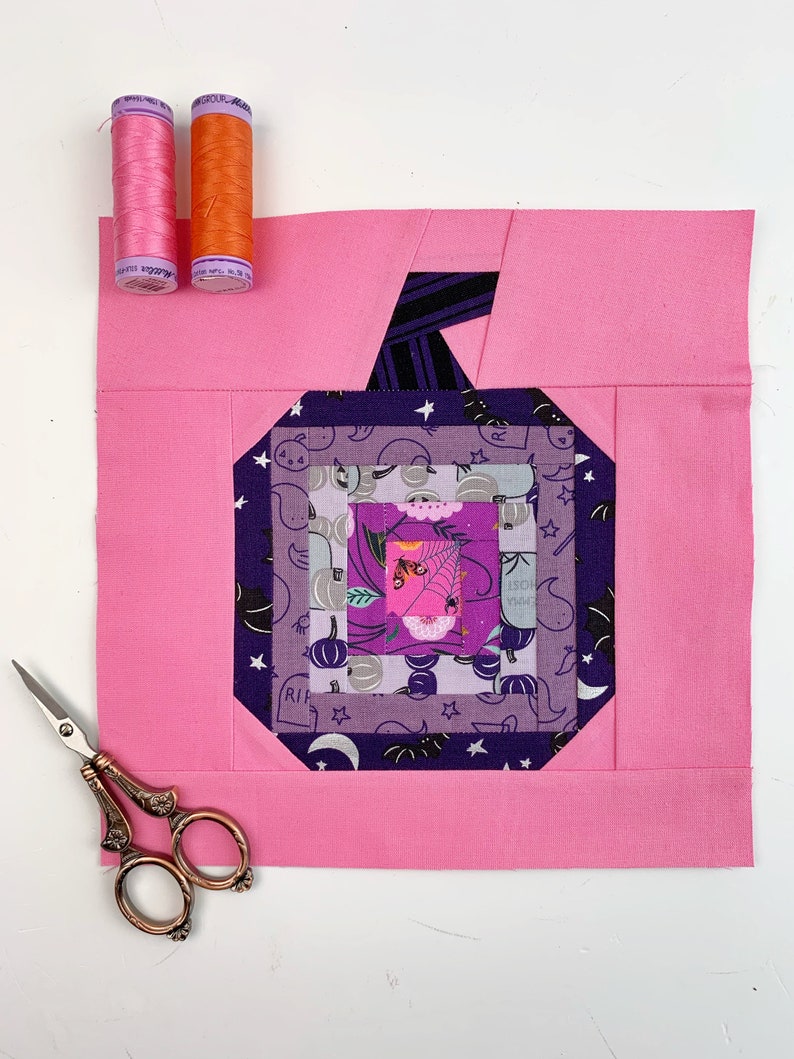 log cabin pumpkin quilt blocks in pink and purple colors on pink background.log cabin pumpkin quilt block pattern in 5 different sizes, from 4x4 inch for ornaments to 6x6, 8x8, 10x10 and 12x12 inches for all sorts of amazing Halloween sewing projects. Use your favorite fabrics to fussy cut the center and turn these amazing beauties into your own pumpkin patch.