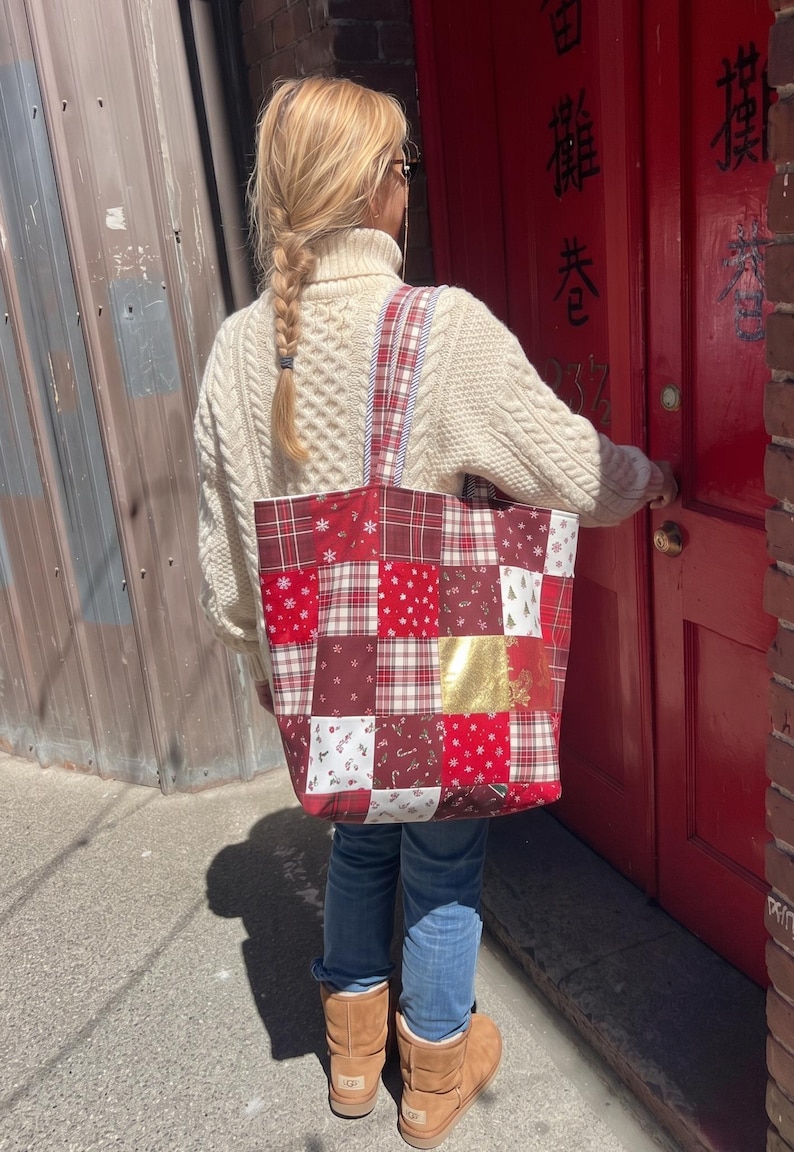 May include: A patchwork tote bag featuring a variety of red, white, and gold fabric squares with holiday-themed patterns including snowflakes, candy canes, and plaid designs, equipped with two matching fabric shoulder straps.