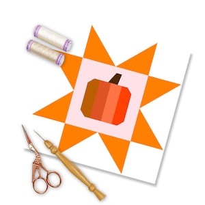 Può includere: Un blocco di tessuto bianco con un design a stella arancione. Il centro del blocco presenta un quadrato rosa con un design a zucca. La zucca è realizzata in tessuto arancione, rosso e marrone. Ci sono due bobine di filo bianco e un paio di forbici dorate su una superficie di legno.