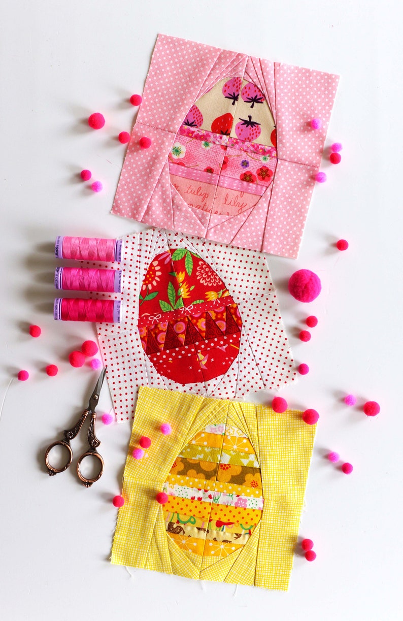 May include: Three fabric patchwork squares with a pink, red, and yellow background. Each square features a different design of an egg with a variety of colorful patterns. The squares are surrounded by pink pom-poms.