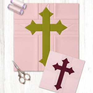 Puede incluir: Dos cuadrados de tela rosa con diseños de cruz, uno verde y otro burdeos, están sobre una superficie de madera blanca. También hay dos carretes de hilo y unas tijeras, lo que sugiere un proyecto de acolchado o costura.