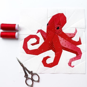 May include: A red and white fabric octopus quilt block with a geometric design. The octopus has a detailed pattern, and the image includes red thread spools and decorative scissors.