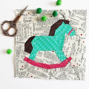 May include: A patchwork rocking horse made from fabric scraps with a teal, brown, pink, and white color scheme. The fabric has a vintage recipe print with red stars.