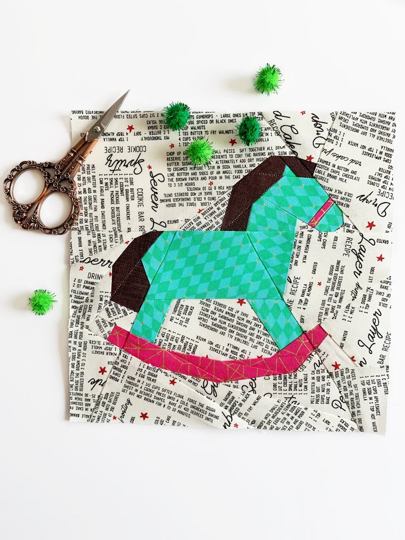 May include: A patchwork rocking horse made from fabric scraps with a teal, brown, pink, and white color scheme. The fabric has a vintage recipe print with red stars.