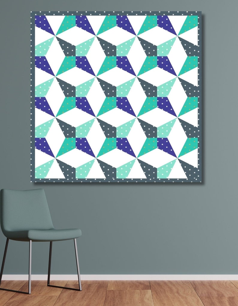 Kaleidoscope quilt pattern in green and blue colors hanging on a teal colored wall with a teal colored chair in the front