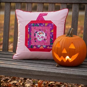 Log cabin pumpkin quilt block, turned into an amazing pillow case with red piping on a wooden bench with a jack o lantern pumpkin.
log cabin pumpkin quilt block pattern in 5 different sizes, from 4x4 inch for ornaments to 6x6, 8x8, 10x10 and 12x12 inches for all sorts of amazing Halloween sewing projects. Use your favorite fabrics to fussy cut the center and turn these amazing beauties into your own pumpkin patch.