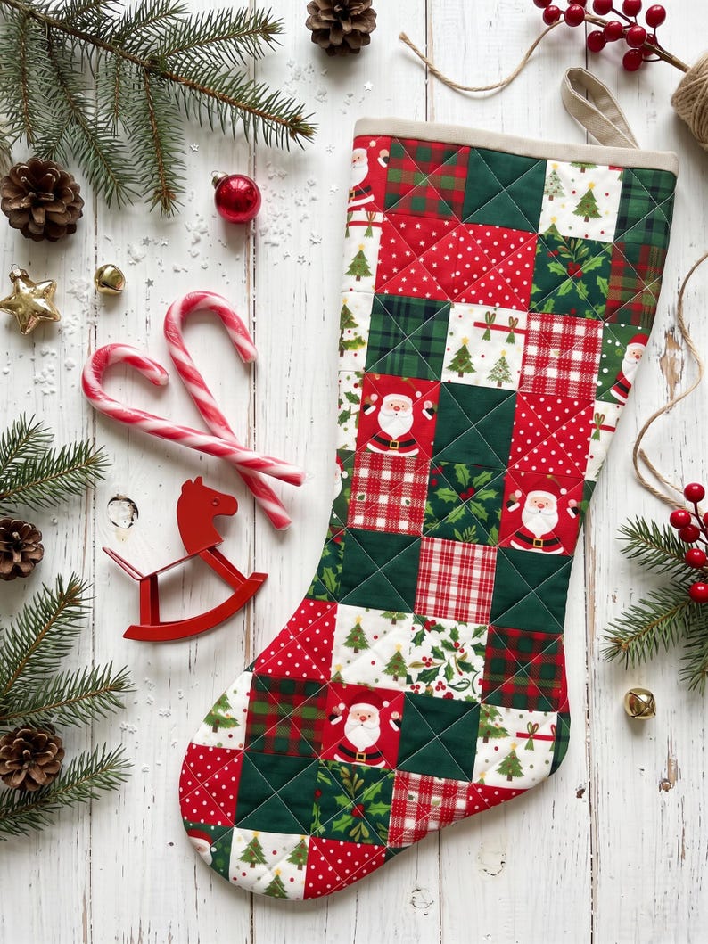May include: A quilted Christmas stocking featuring a patchwork design of red, green, and white squares. The fabric patterns include illustrations of Santa Claus, Christmas trees, holly leaves, red and white polka dots, and plaid.