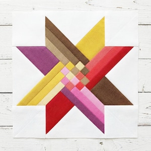 Puede incluir: Un bloque de edredón de estrella colorido con un diseño geométrico. La estrella presenta segmentos amarillos, rojos, rosas, morados y marrones, sobre un fondo blanco. El bloque es cuadrado y parece hecho a mano, mostrando un estilo patchwork.