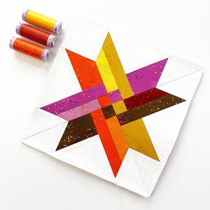 Puede incluir: Un bloque de edredón en forma de estrella con formas geométricas en naranja, amarillo, morado y marrón. Tres carretes de hilo en colores a juego están colocados a la izquierda. El bloque de edredón está sobre un fondo blanco.