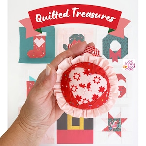 May include: A round fabric ornament featuring a central heart pattern with red star motifs on a light pink background, surrounded by a ruffled light pink border and a red and white checkered hanging loop, set against a background of quilted squares.