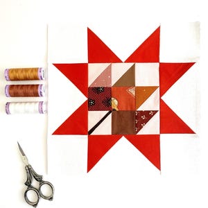 May include: A patchwork quilt block with a red and white star pattern. The central design incorporates squares of patterned fabric in brown, orange, and pink hues. Three spools of thread and a pair of scissors are also present.