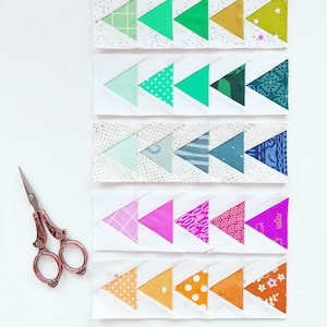 May include: Five rows of fabric triangles sewn together in a chevron pattern. Each row features a different color scheme, including green, blue, pink, and orange. The fabric triangles have various patterns, including polka dots, stripes, and floral prints.