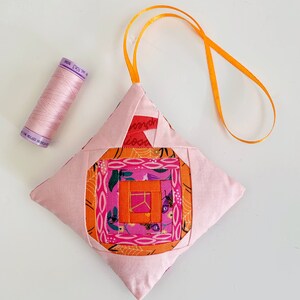 log cabin pumpkin ornament in pink and orange.log cabin pumpkin quilt block pattern in 5 different sizes, from 4x4 inch for ornaments to 6x6, 8x8, 10x10 and 12x12 inches for all sorts of amazing Halloween sewing projects. Use your favorite fabrics to fussy cut the center and turn these amazing beauties into your own pumpkin patch.