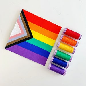 May include: A rainbow-colored fabric square with a white triangle in the corner, and a set of spools of thread in rainbow colors.
