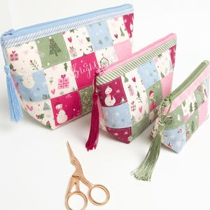May include: Three zippered pouches in descending sizes featuring a patchwork pattern of snowmen, Christmas trees, and gifts in pink, green, and blue. Each pouch has a matching tassel and a pair of rose gold stork-shaped embroidery scissors.