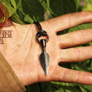 May include: A black leather cord necklace with a small, black metal spearhead pendant. The pendant is approximately 5 cm long and has a pointed tip.