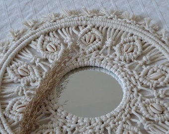 May include: A white macrame mirror with a round mirror in the center. The macrame is decorated with small white seashells.