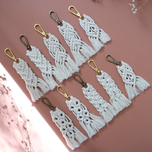 May include: Ten white macrame keychains with gold and bronze key rings. Each keychain has a different pattern and is numbered 1 through 10.