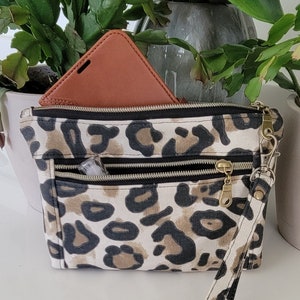 May include: A small leopard print zippered pouch with a wrist strap. The pouch has two zippered compartments and a brown leather phone case inside.