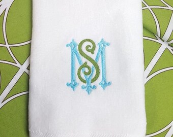 May include: White hand towel with a green and blue embroidered monogram of the letters "MS".