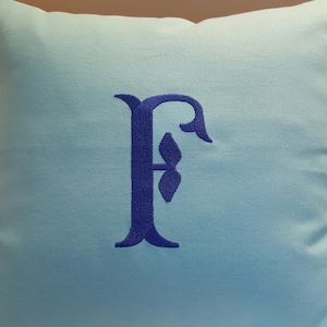 May include: A light blue throw pillow with a blue embroidered letter F in a decorative font.