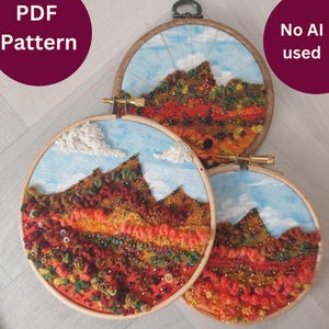 May include: Three embroidery hoops featuring colourful wool and bead embellishments depicting a mountain landscape. The hoops are of different sizes, with the largest hoop showing a blue sky with white clouds.