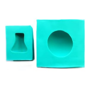 May include: Two silicone molds for making crafts. One mold is a square with a round indentation and the other is a square with a bell-shaped indentation.