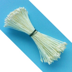 Puede incluir: Un paquete de alambre floral blanco con puntas de purpurina iridiscente. El alambre está atado con una atadura de torsión negra.