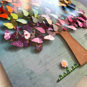 May include: A colorful card with a 3D paper butterfly tree. The tree is made of many butterflies in shades of purple, blue, green, yellow, orange, and red. A small pink flower with green leaves is at the base of the tree.