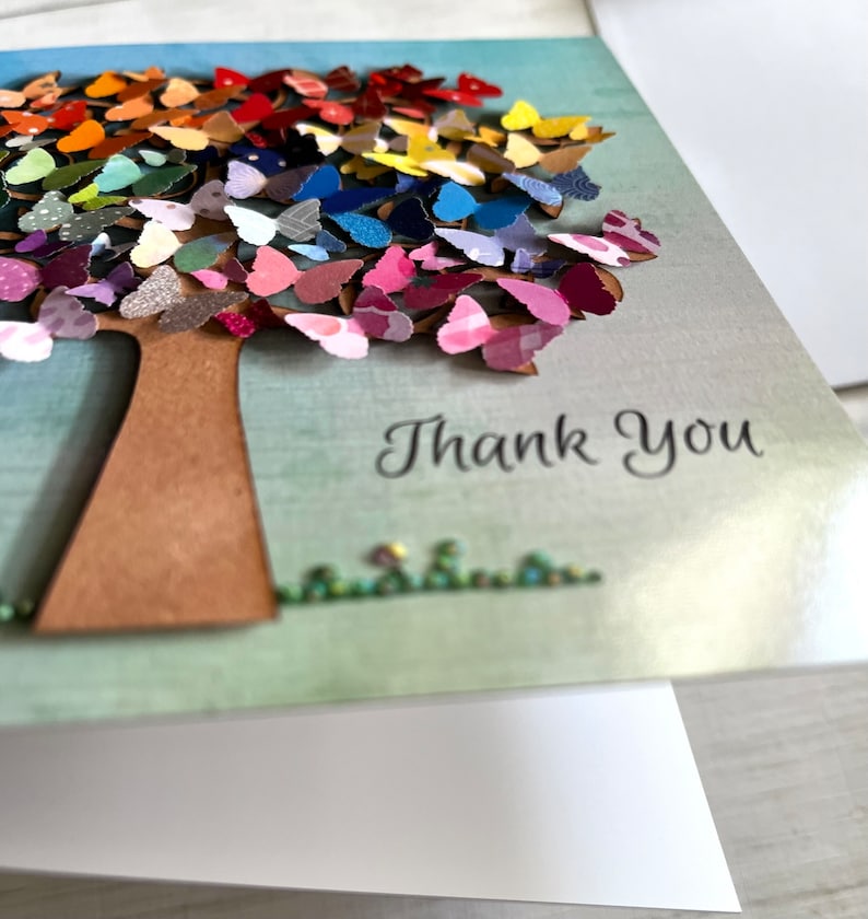 May include: A handmade thank you card featuring a colorful paper butterfly tree with the words "Thank You" printed below.