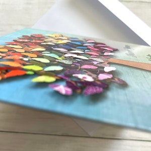 May include: A greeting card with a blue background and a colorful butterfly tree design. The tree is made of paper butterflies in various colors and patterns. The card has the text "Happy Day" on the front.