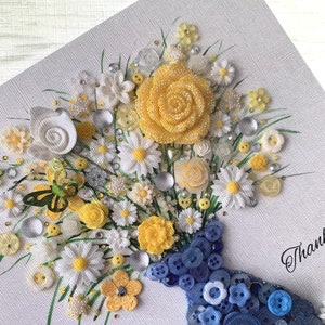 May include: A handmade card featuring a bouquet of yellow and white flowers in a blue button vase. The flowers are made of fabric and buttons, and the vase is made of buttons. The card has the word "Thank" written on it.
