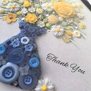 May include: A blue button vase filled with a bouquet of yellow and white flowers. The flowers are made of fabric and buttons. The vase is decorated with blue buttons. The background is white with the text "Thank You".