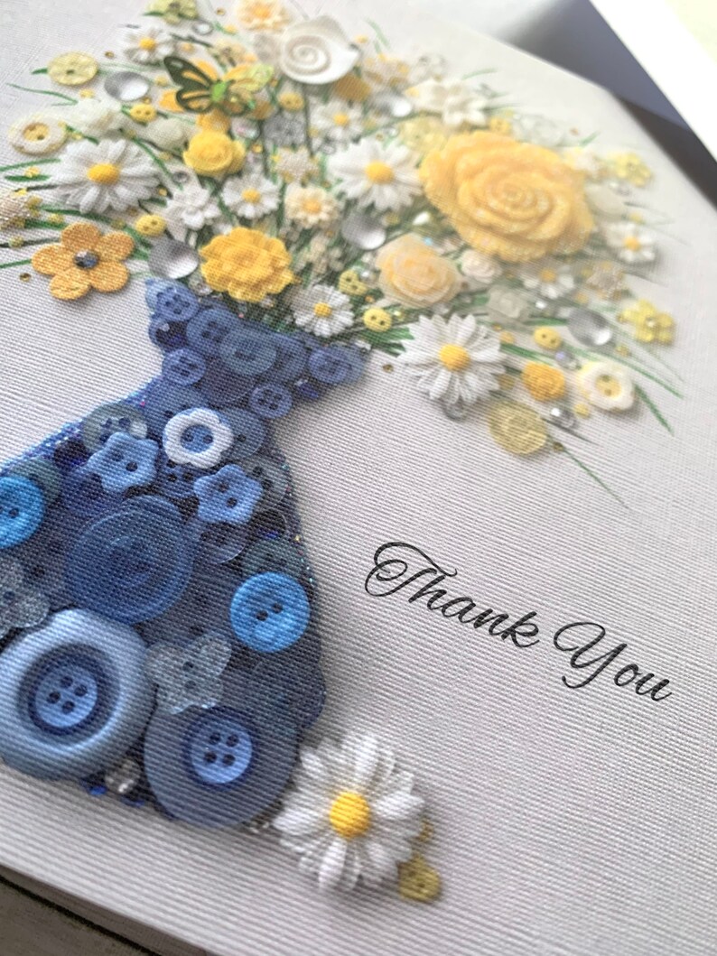 May include: A blue button vase filled with a bouquet of yellow and white flowers. The flowers are made of fabric and buttons. The vase is decorated with blue buttons. The background is white with the text "Thank You".