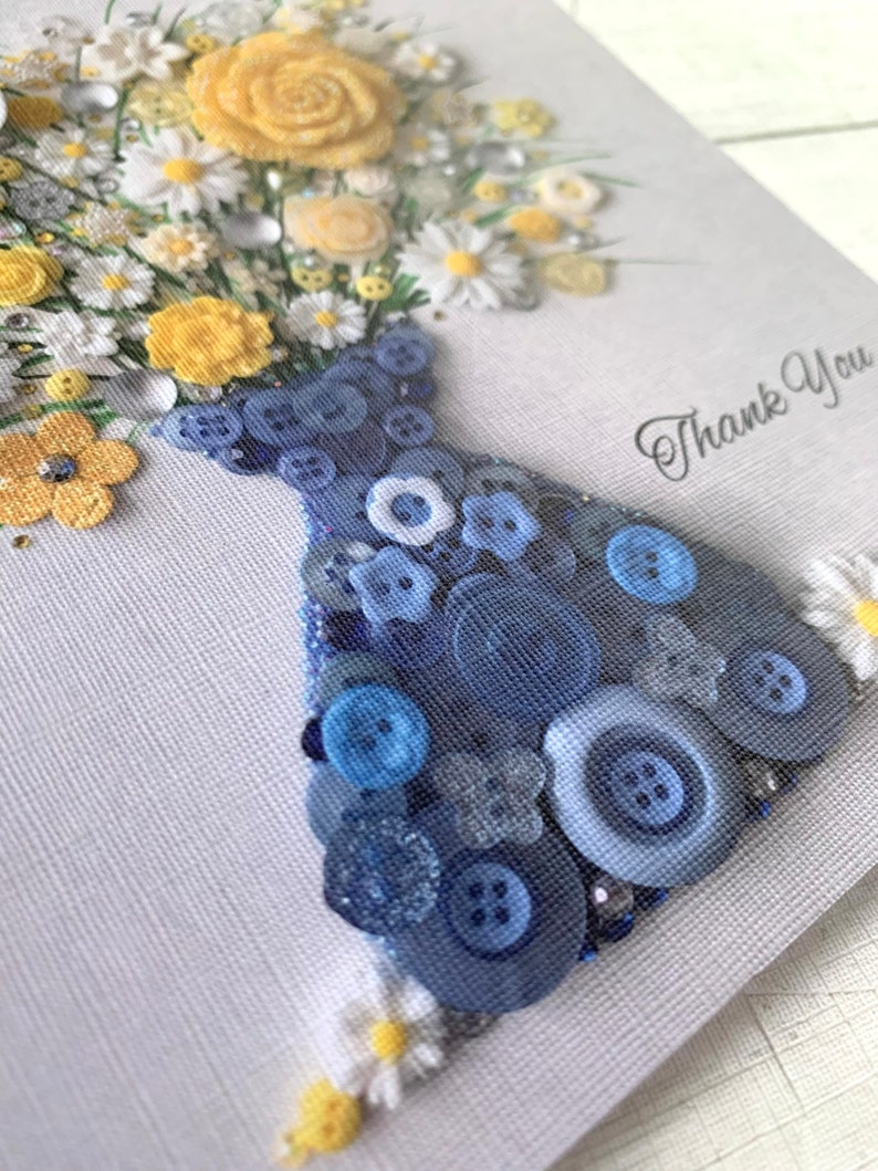 May include: A handmade thank you card featuring a bouquet of yellow and white flowers in a blue button vase. The card has a white background with the words "Thank You" written in black.
