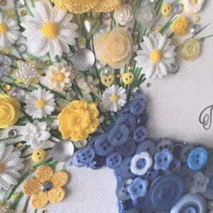 May include: A white canvas with a bouquet of yellow and white flowers made from buttons and other embellishments. The flowers are arranged in a blue button vase.