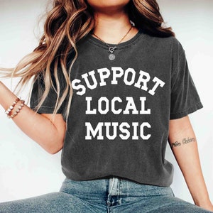 May include: A charcoal grey t-shirt with the text "SUPPORT LOCAL MUSIC" printed in white.