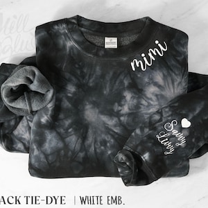 May include: A black and gray tie-dye crewneck sweatshirt featuring white embroidered text that reads Mimi on the upper chest and Savvy Livy with a small heart symbol on the sleeve. The garment has a soft fleece interior lining.