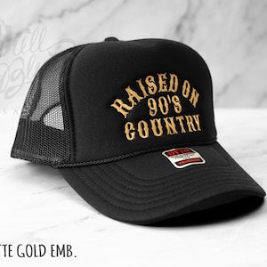 May include: Black trucker hat with a mesh back and a curved brim. The front of the hat features the embroidered text "RAISED ON 90'S COUNTRY" in gold. The text "MATTE GOLD EMB." is printed at the bottom.