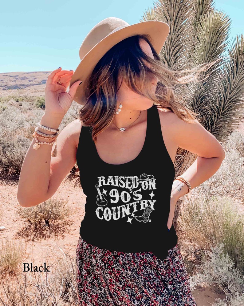K&ouml;nnte beinhalten: Schwarzes Tanktop mit einem wei&szlig;en Aufdruck, der "Raised on 90's Country" mit einer Gitarre, einem Cowboyhut und Cowboystiefeln zeigt.