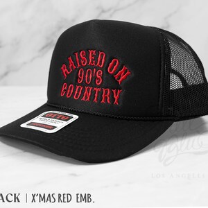 May include: Black trucker hat with a mesh back and a curved brim. The front of the hat features the embroidered text "RAISED ON 90'S COUNTRY" in red. The hat has a snapback closure and a tag that reads "OTTO".