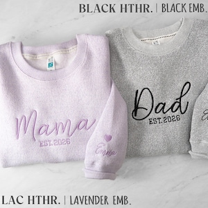 May include: A lilac heather sweatshirt embroidered with Mama and EST. 2026, and a black heather sweatshirt embroidered with Dad and EST. 2026. Both sleeves feature the name Emma and a small heart icon in matching thread colors.