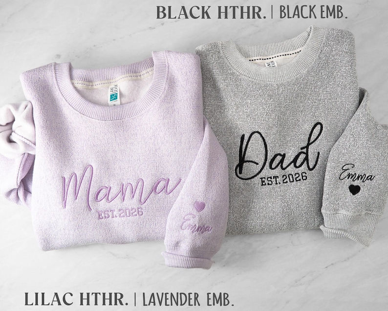 May include: A lilac heather sweatshirt embroidered with Mama and EST. 2026, and a black heather sweatshirt embroidered with Dad and EST. 2026. Both sleeves feature the name Emma and a small heart icon in matching thread colors.